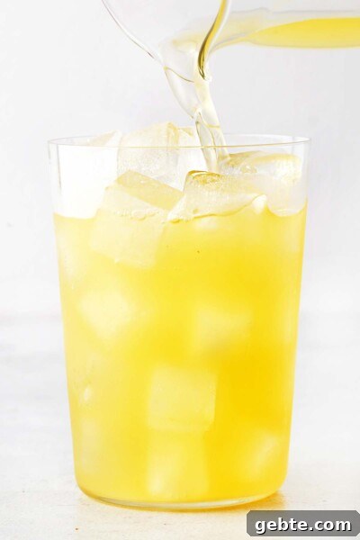 Pineapple Iced Tea Recipe — Tropical Summer Drink 8 Pineapple Iced Tea being poured into clear cup filled with ice.