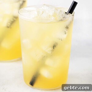 Pineapple Iced Tea Recipe — Tropical Summer Drink 10 Two glasses are filled with ice cubes and pineapple iced tea, with a straw inside.