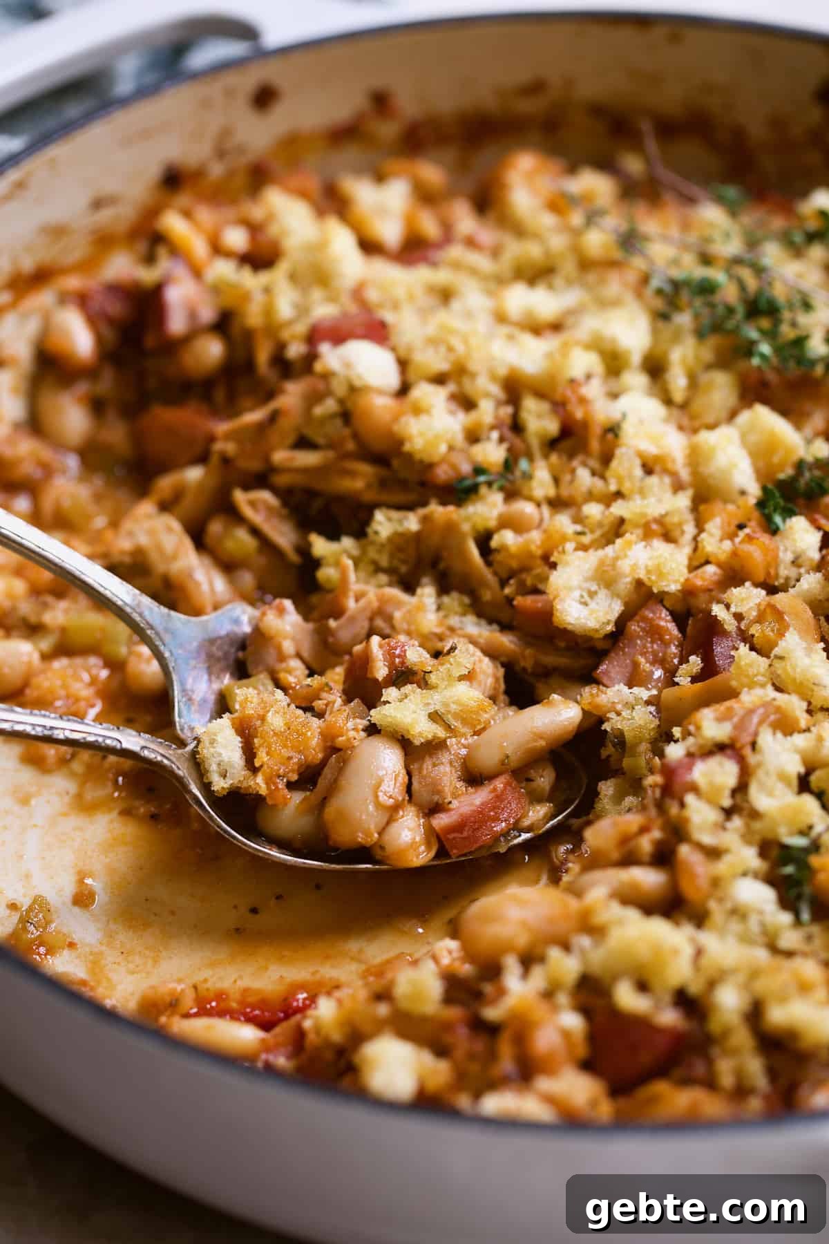 Close-up photo of cassoulet being served from white cast iron skillet.