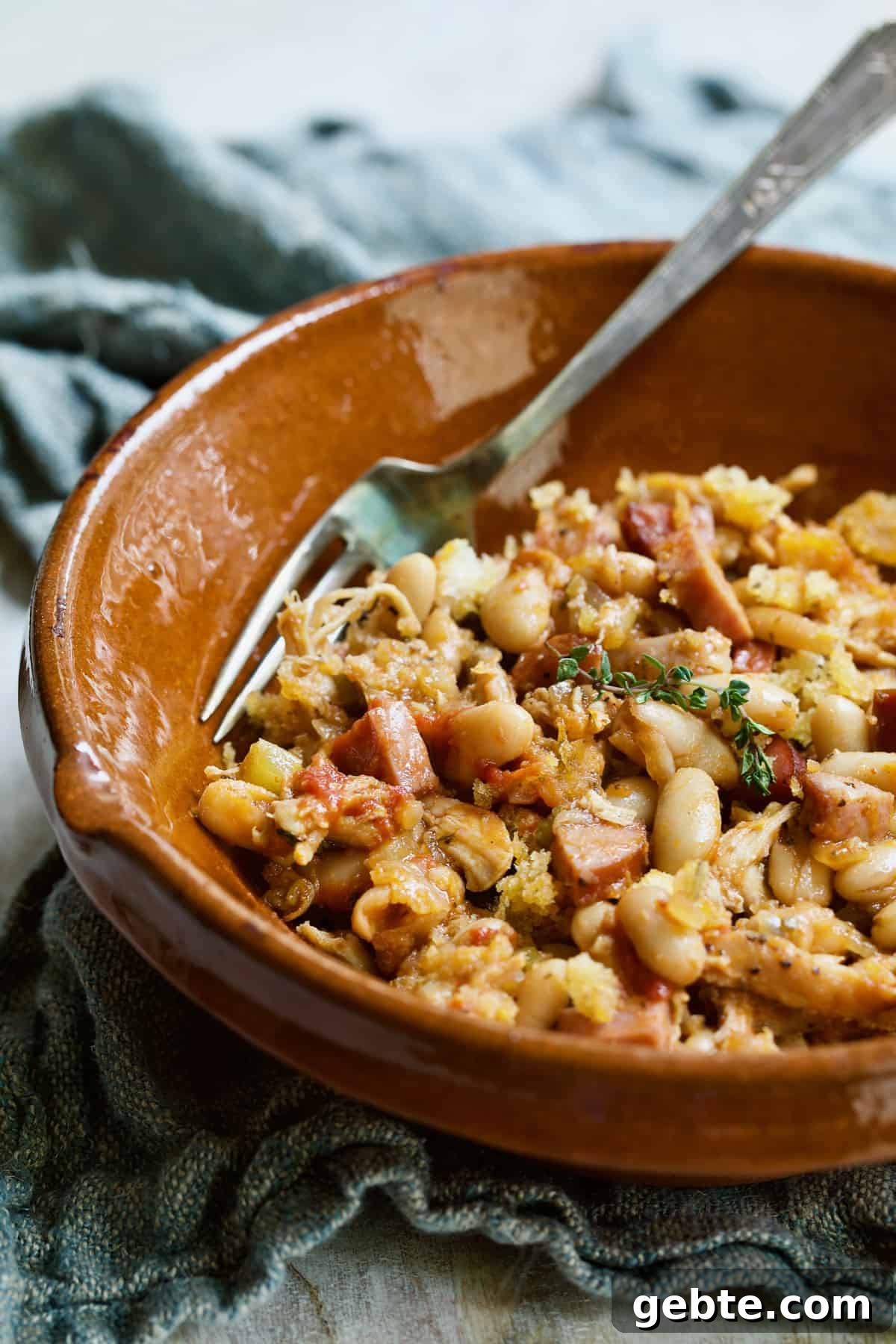 Photo of one serving of Easy Weeknight Chicken and Sausage Cassoulet in red clay bowl.