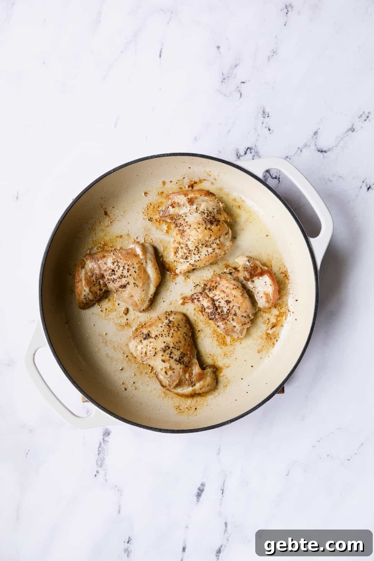 Photo of four boneless skinless chicken thighs in white cast iron skillet.