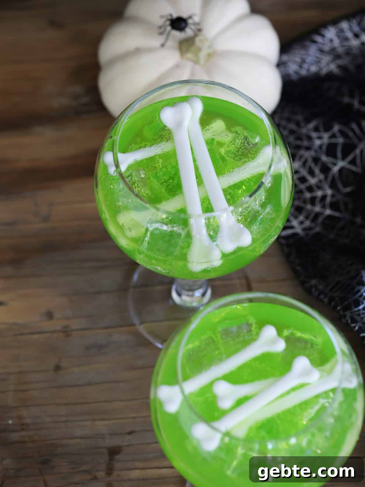 Looking down on two glasses with green Midori vodka drinks garnished with white bones.