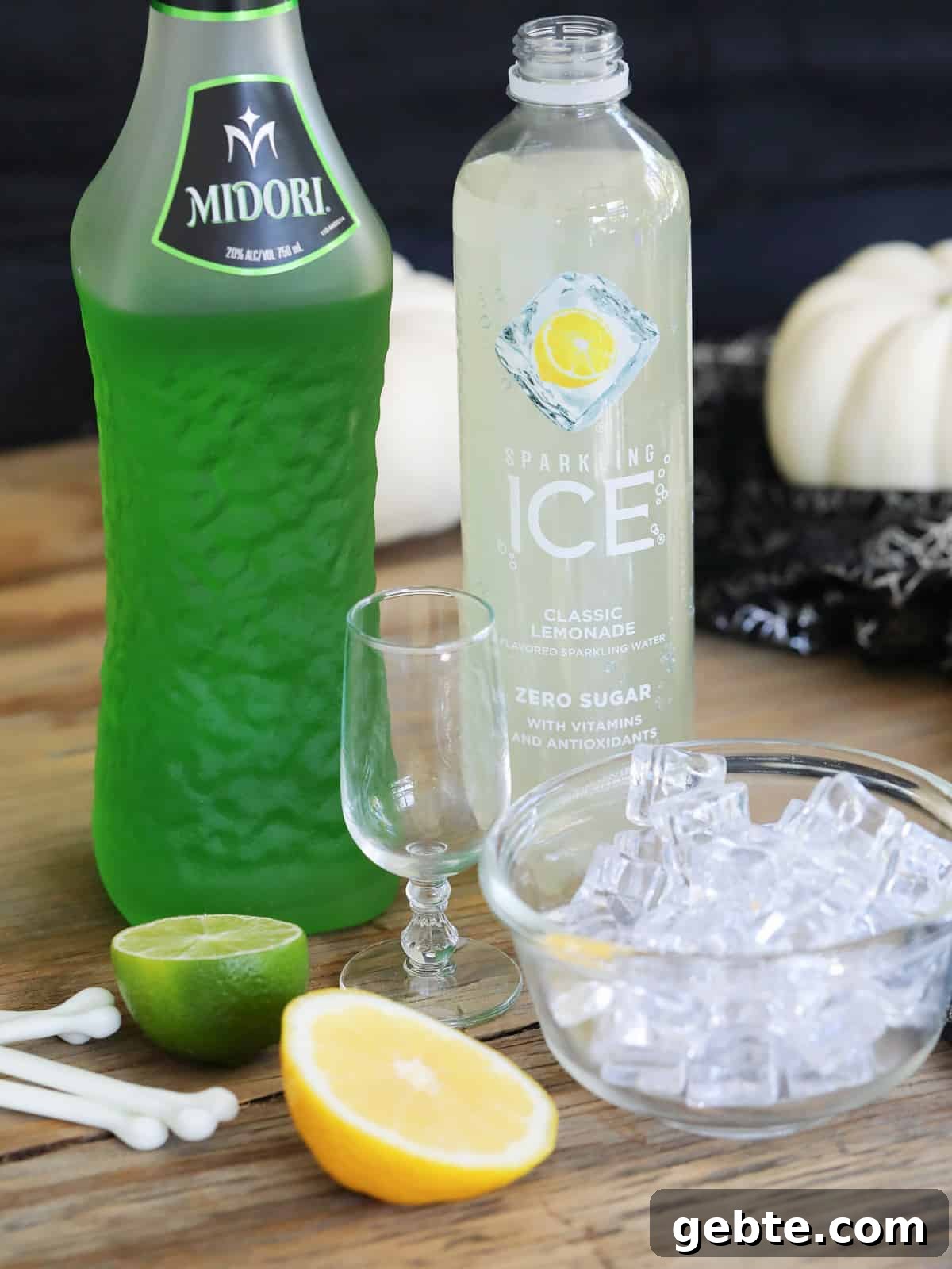 Ingredients for Midori sours including Midori, ice, lemon, lime, vodka, sparkling water on a table.