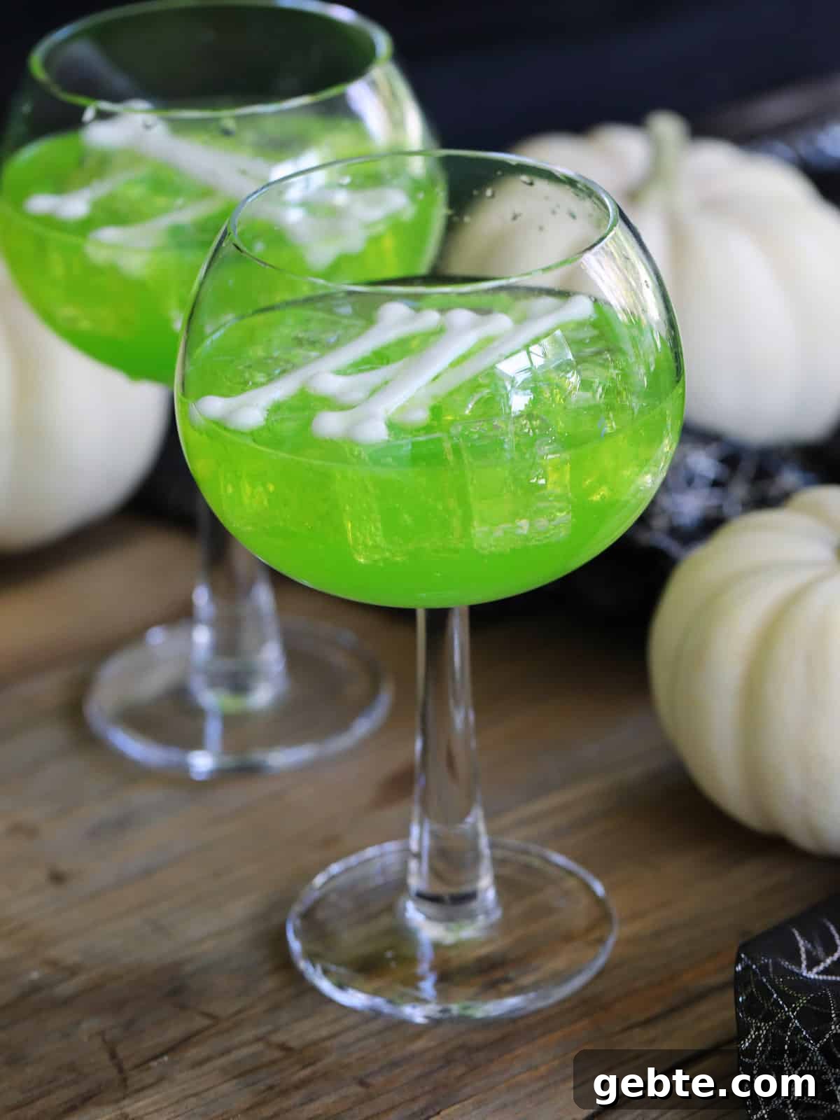 Two tall glasses filled with green drinks for a Halloween party and white bones as a garnish.