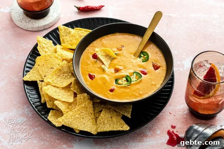 Bowl of bright orange queso dip on a plate with chips