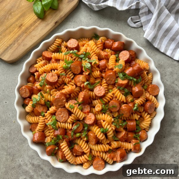 A white round dish filled with Sausage Pasta garnished with fresh basil.