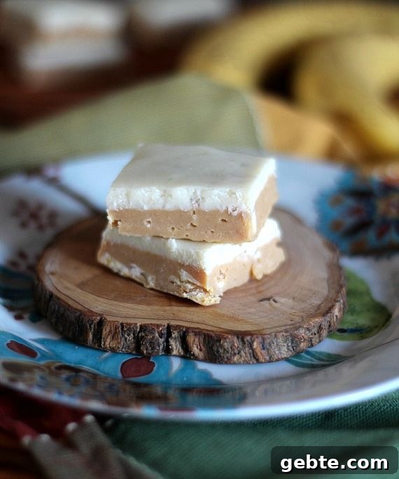 Two squares of Peanut Butter Banana Fudge stacked on a piece of wood on a plate