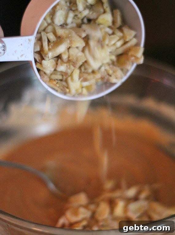 Banana chips being added to peanut butter fudge ingredients in a double boiler