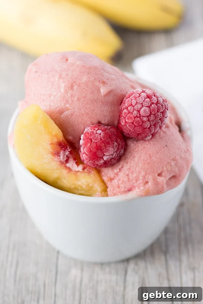 A white cup of raspberry peach nice cream with bananas and white napkin in the background.