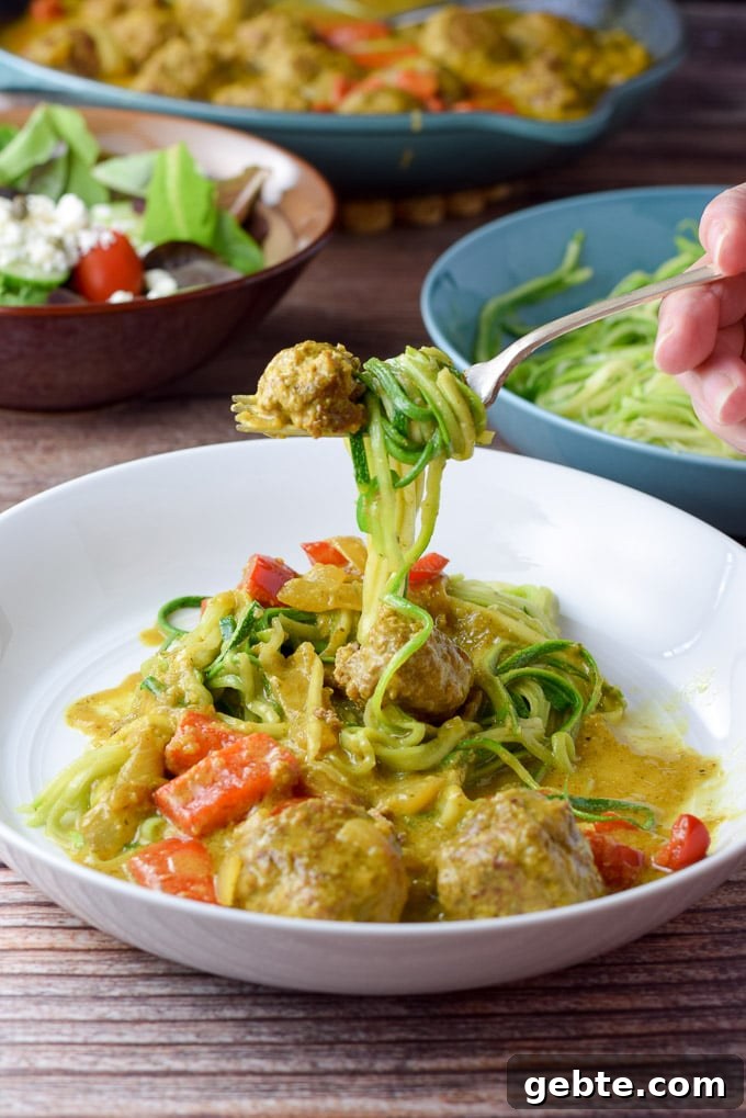 Forkful of twirled zoodles and a piece of meatball. There is a salad and the pan of meatballs in the background