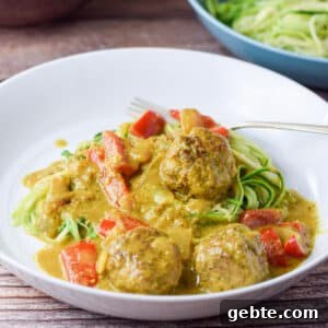 A white plate with meatballs in a curry sauce on zoodles - square