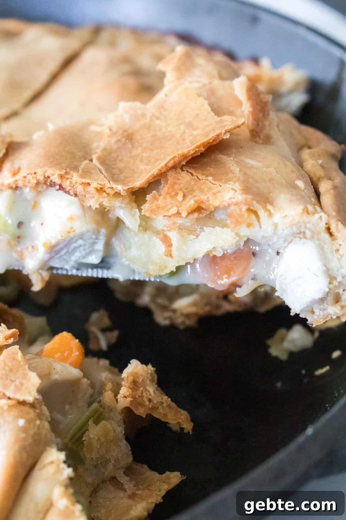 vertical shot of a piece of chicken pot pie made with pie crust being lifted out of cast iron skillet