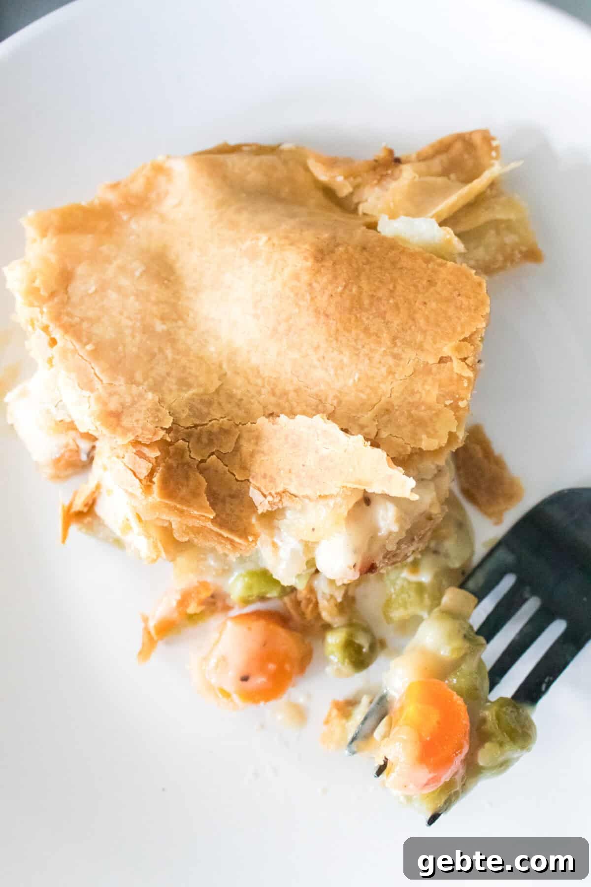 close up vertical shot of chicken pot pie on white plate with bite on black fork