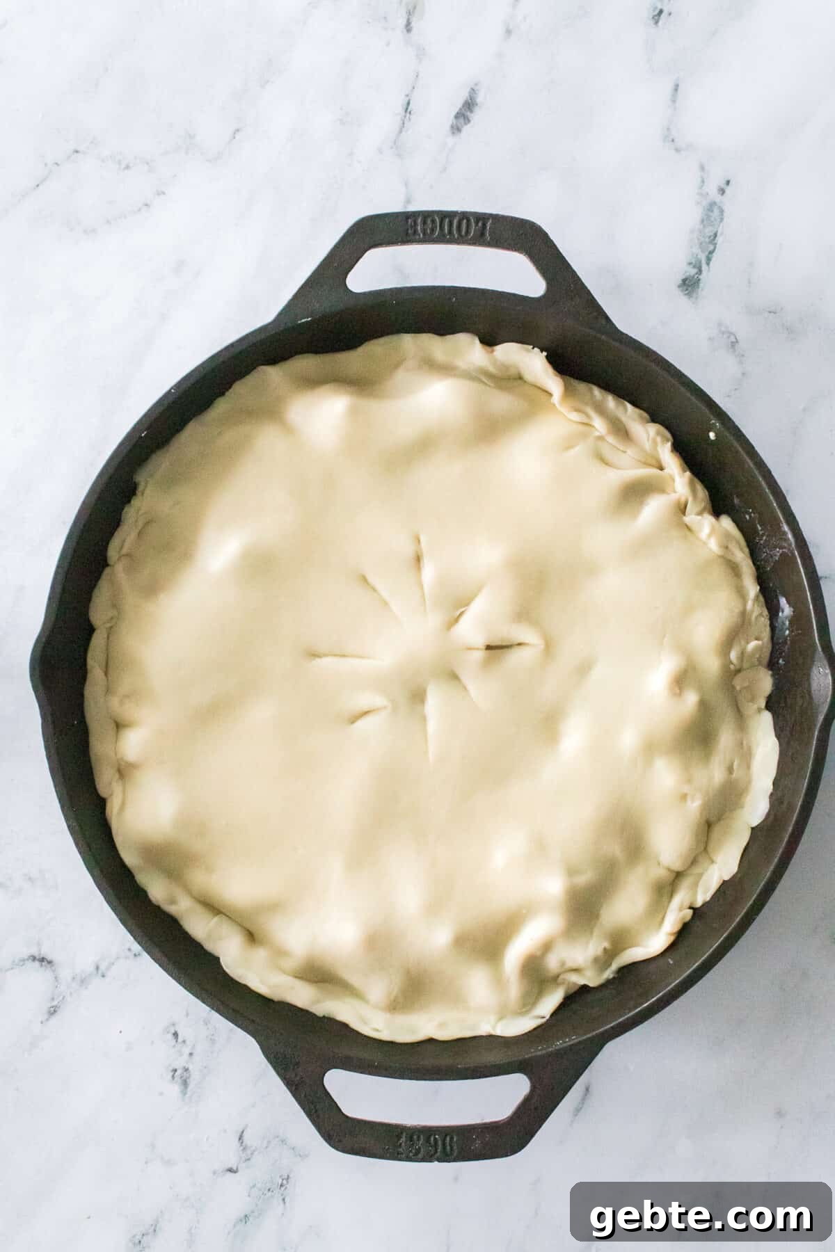overhead vertical shot of chicken pot pie in cast iron skillet with slits cut in pie dough previous to baking