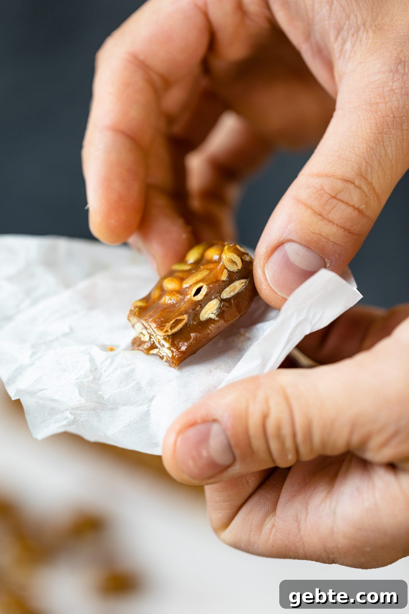 Hand holding pumpkin spice caramels in white wrapper with extra caramels in background on a gray surface