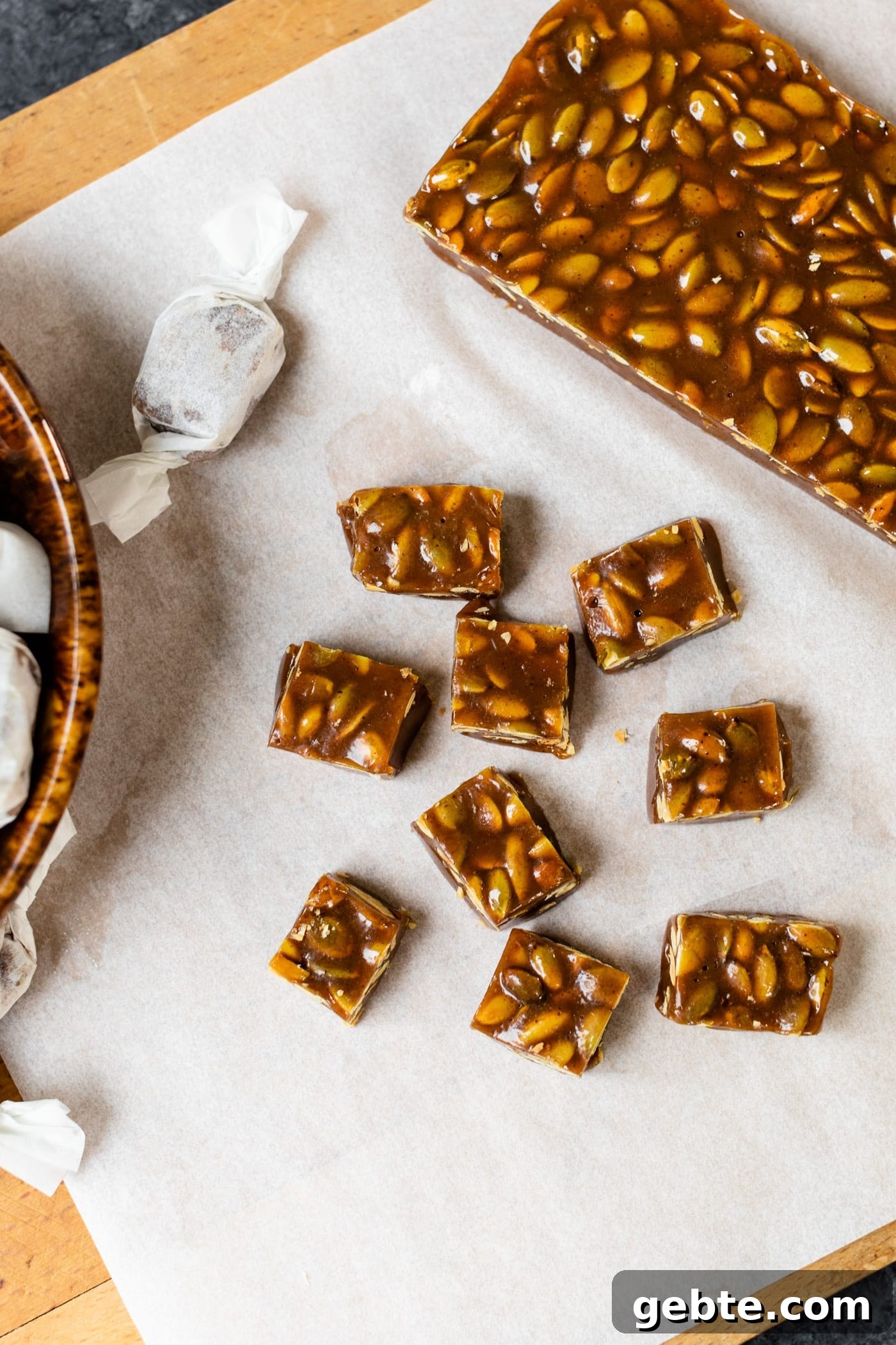 Top down view of pumpkin spice caramels sitting on white parchment on board with bowl containing wrapped caramels all on gray slate surface