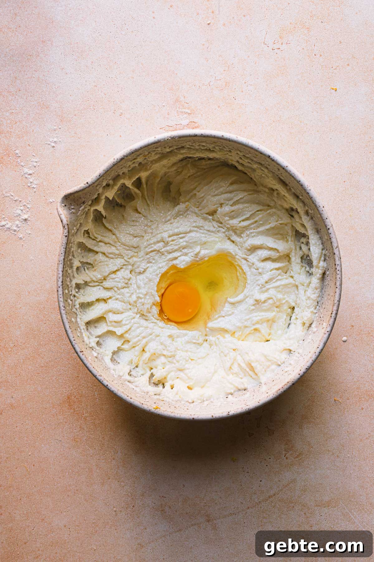 A bowl with creamed butter and sugar and a whole egg.