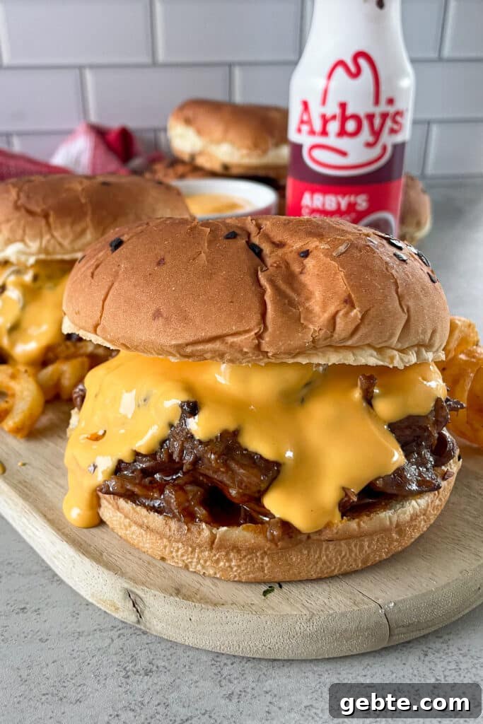 copycat Arby's beef and cheddar sandwich on a serving board with curly fries and a bottle of Arby's sauce for serving.