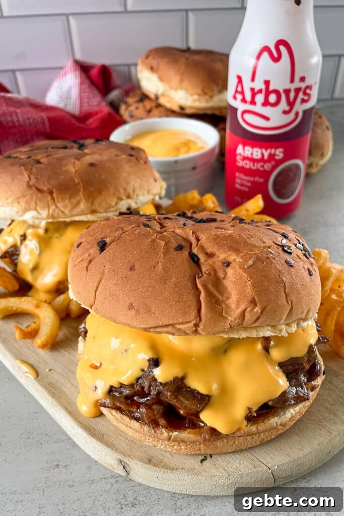 copycat Arby's beef and cheddar sandwich on a serving board with curly fries and a bottle of Arby's sauce for serving.