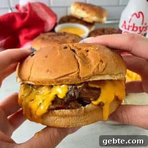 close up photo of Arby's beef and cheddar held in a hand ready to be eaten.