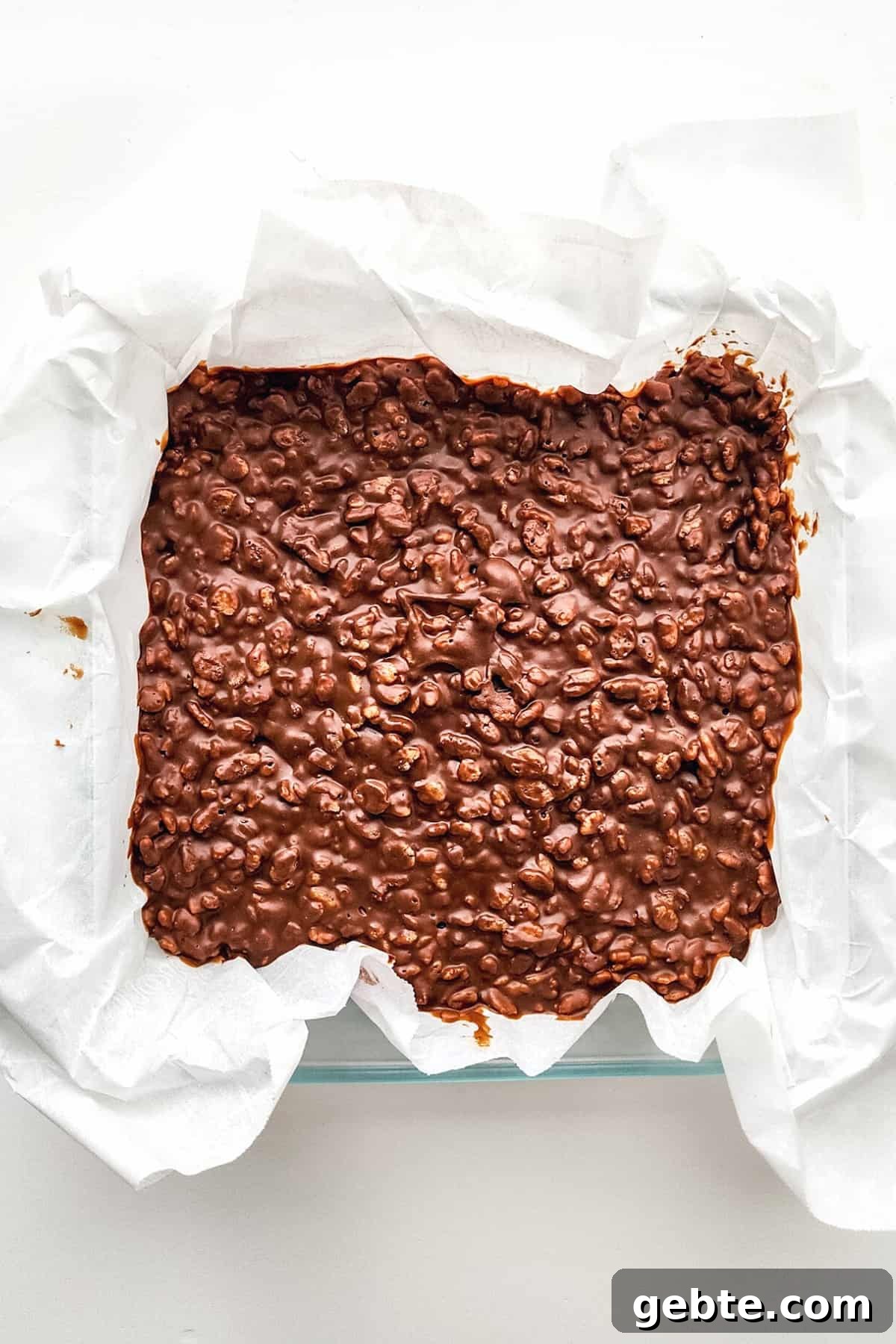 Chilled chocolate peanut butter rice cereal mixture in parchment-lined baking dish.