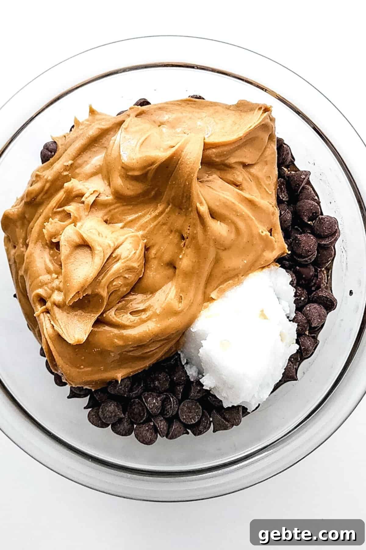 Peanut butter, chocolate chips and coconut oil in glass bowl.