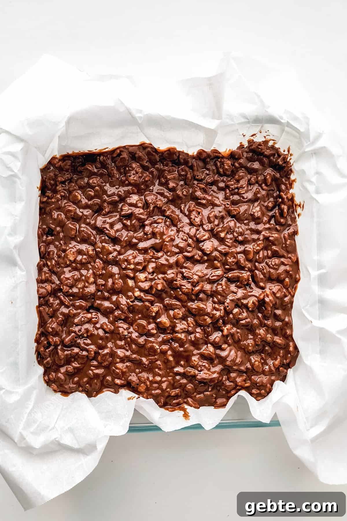 Peanut butter crunch bars mixture in parchment-lined baking dish.