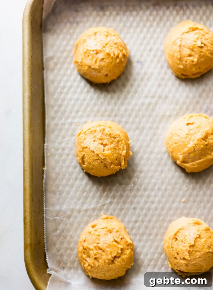 Balls of peanut butter dough on a baking tray lined with parchment.