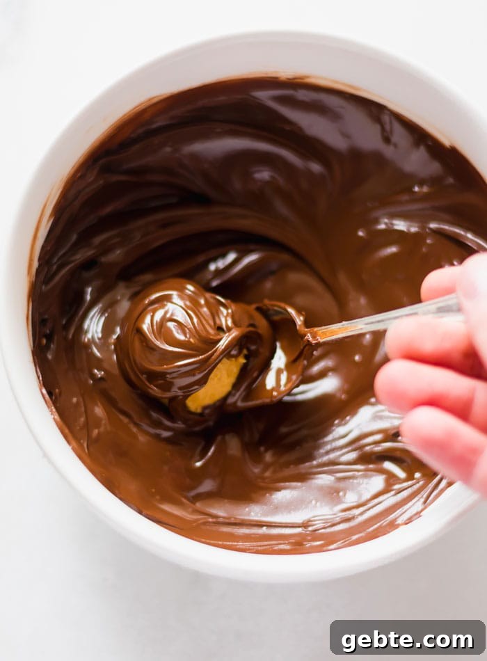 A peanut butter ball being dipped in a bowl of melted chocolate.