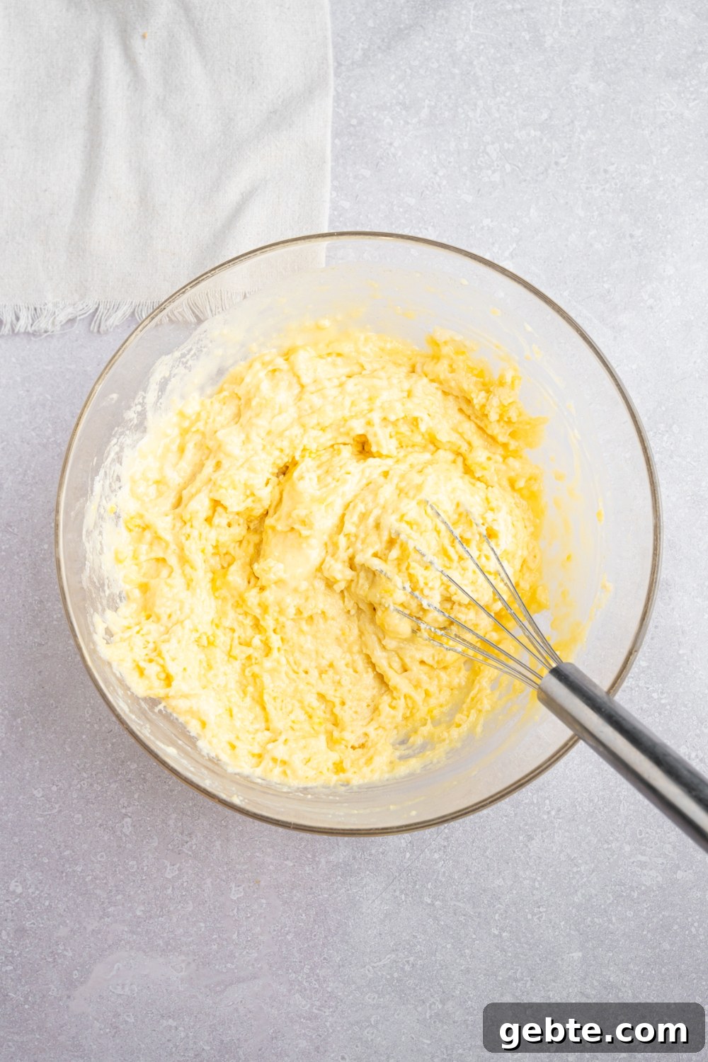 A glass bowl with a whisk mixing Bisquick dough. The bowl is on a white counter with a white napkin.