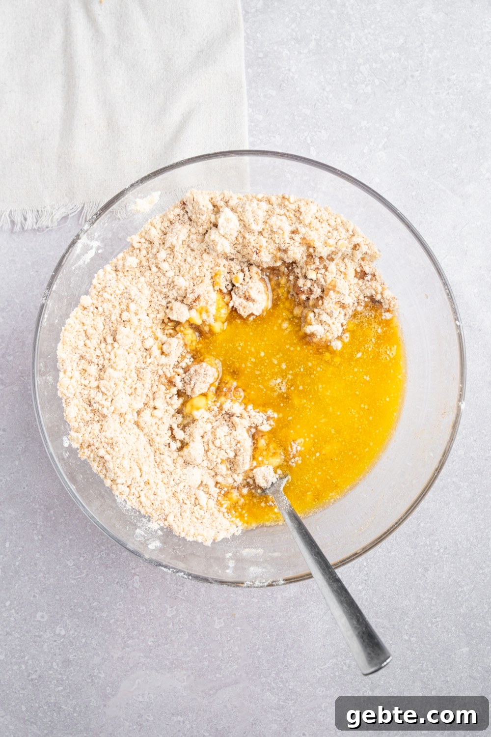 A glass bowl with ingredients to make a coffee cake crumb topping including brown sugar, Bisquick mix, cinnamon, and melted butter.