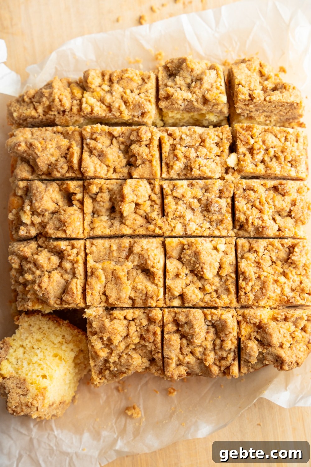 A whole Bisquick coffee cake sliced in squares on a piece of parchment paper over a wooden board. One slice is tipped out of the cake.