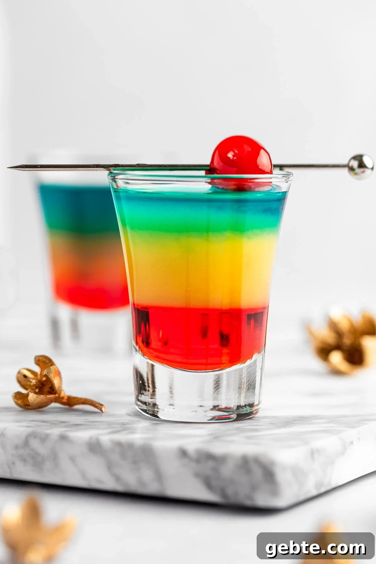 Rainbow shots with red, yellow and blue layers, garnished with a maraschino cherry.