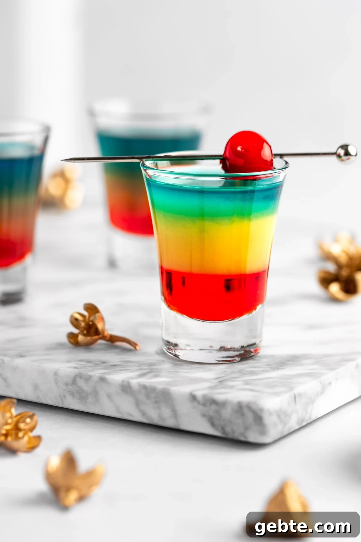 A rainbow shot with colored layers, garnished with a maraschino cherry.