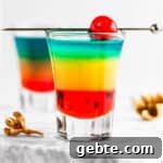 Rainbow shots with red, yellow and blue layers, garnished with a maraschino cherry.