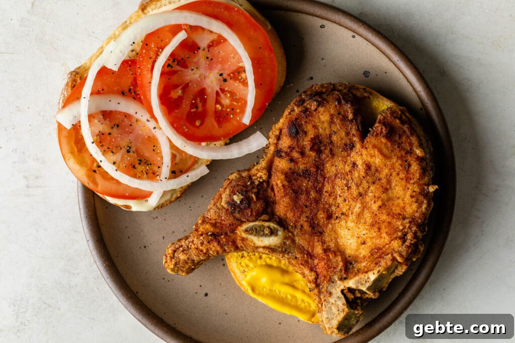 pork chop sandwich with tomato, mustard, and onions on a plate